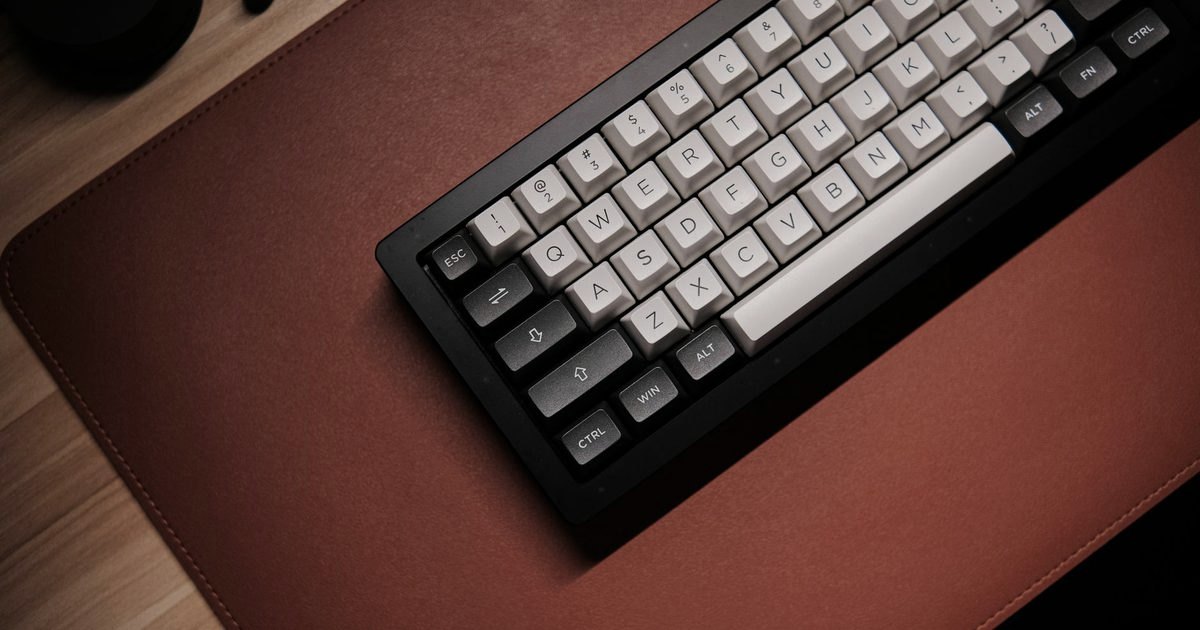 A mechanical keyboard on a brown leather desk mat, top-down