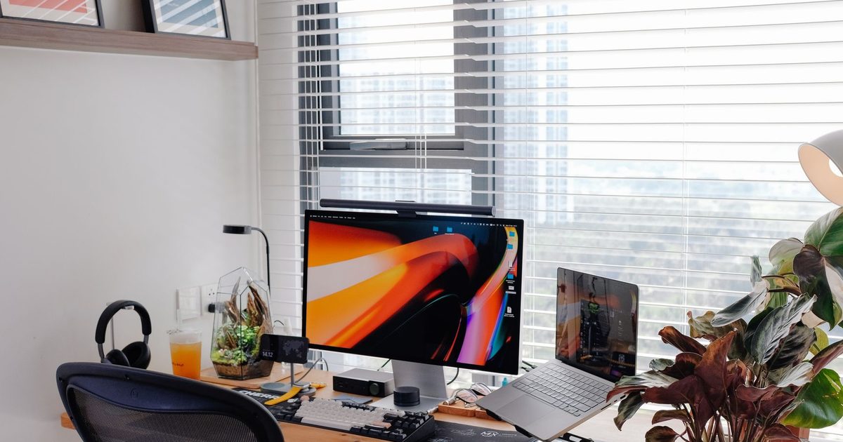 a home office desk with a laptop, monitor and a plant by a window