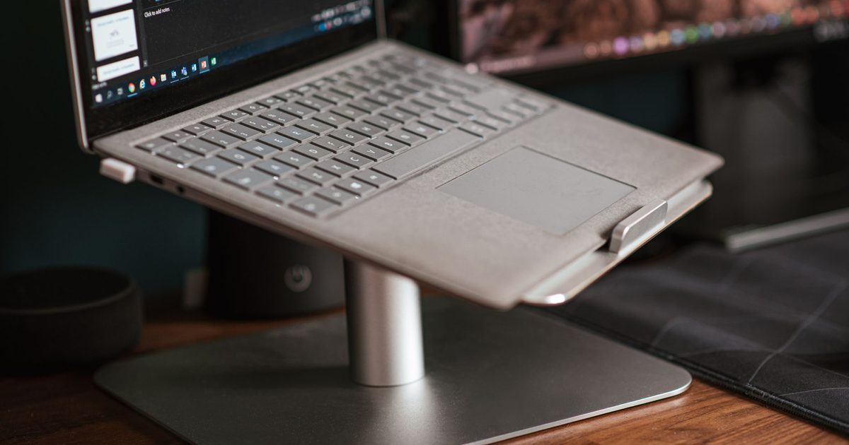 a laptop raised on an aluminium stand on a wooden desk