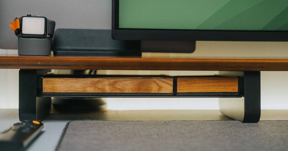 a monitor on a wooden riser shelf with a storage drawer underneath