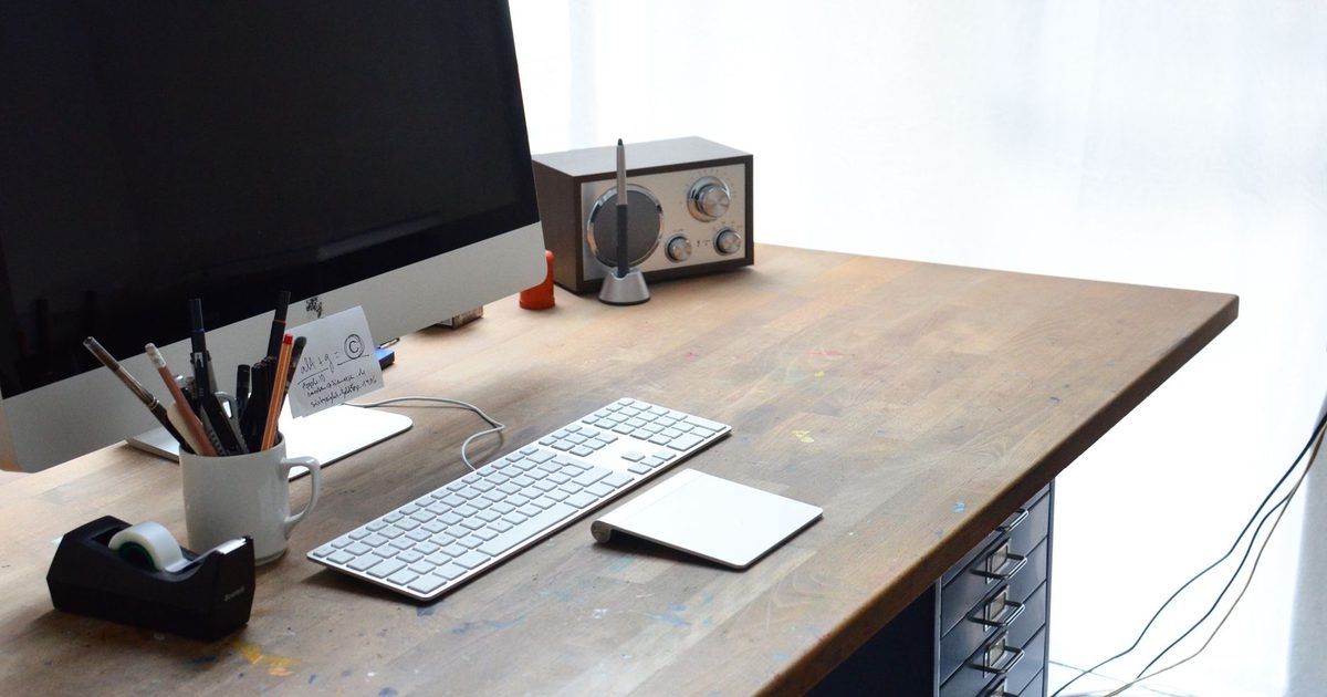 a keyboard and monitor on a wooden desk with cables running underneath