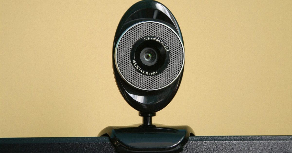 a black clip-on webcam standing against a plain warm background