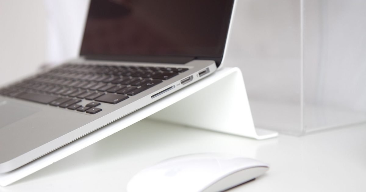 a silver laptop raised on a white stand above a bright desk