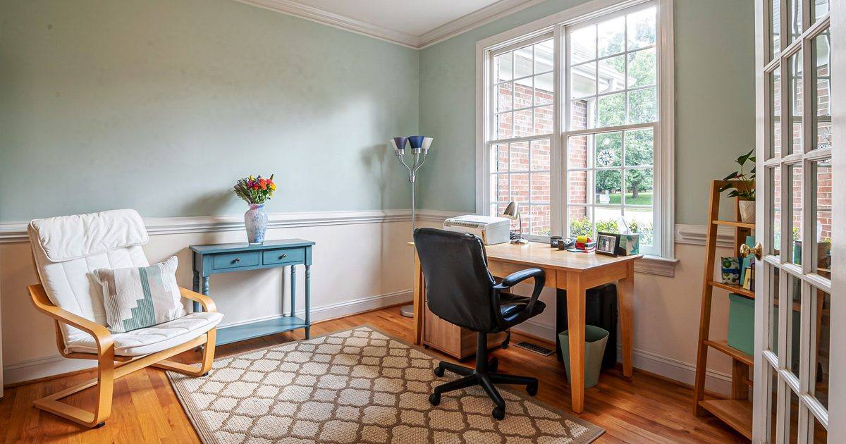 black office chair tucked under a wooden desk by a bright window