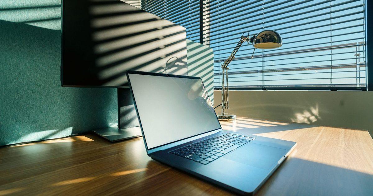 sunlight through venetian blinds falling across a desk with a laptop and monitor