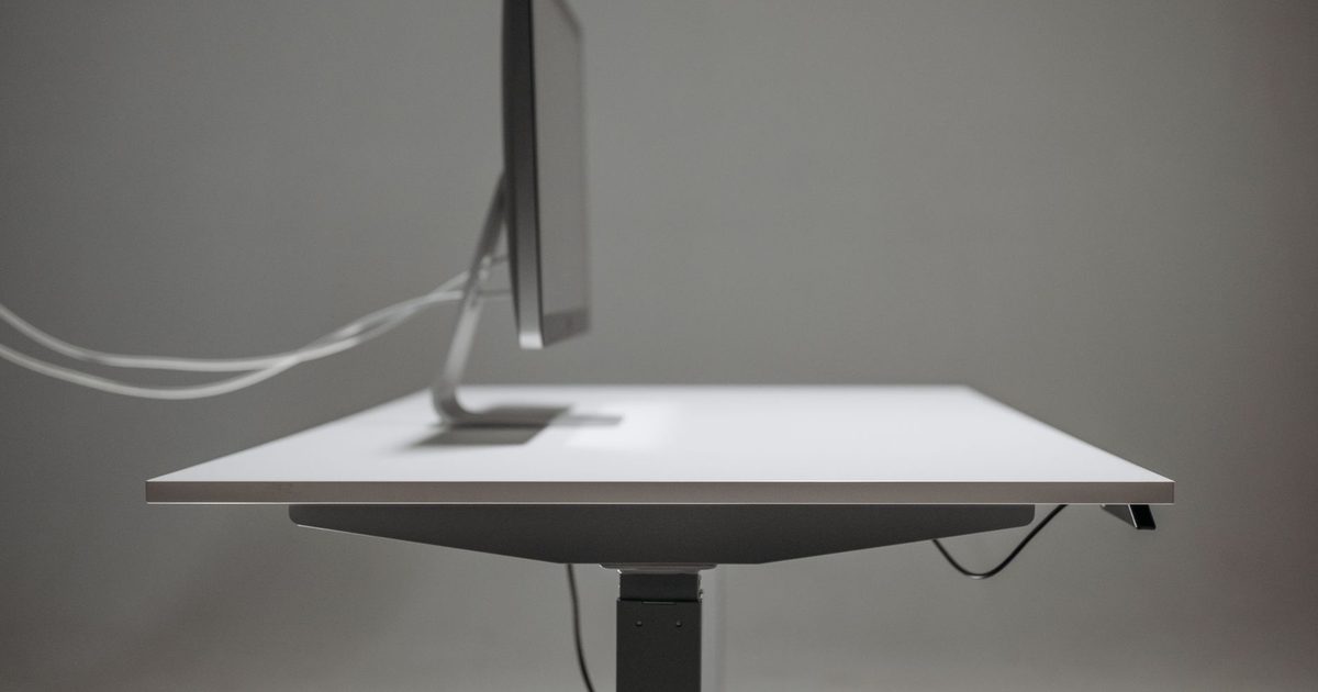 a white height-adjustable standing desk with a monitor seen from the side